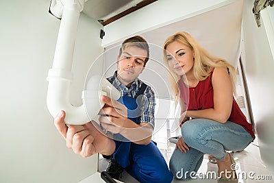 Plumber Showing Damage In Sink Pipe To Woman Stock Photo