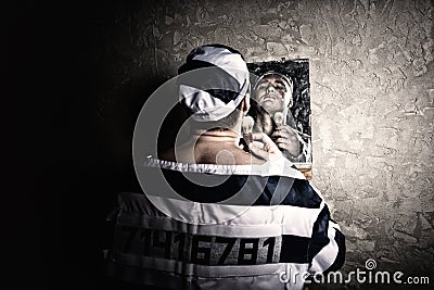 Male prisoner standing with shave brush and looking at his reflection in the mirror in a prison cell Stock Photo