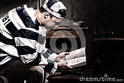 Male prisoner wearing prison uniform reading a book or a bible w Stock Photo