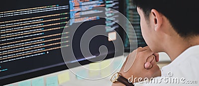 A male programmer sits and watches the code on a computer monitor to verify the program`s execution Stock Photo