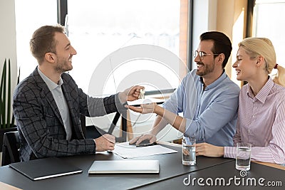 Male realtor give keys to excited Caucasian couple in office Stock Photo