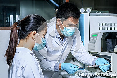 The male researcher prepares a column chromatography cartridge of the LC-MS instrument to analyze and train a female scientist to Stock Photo