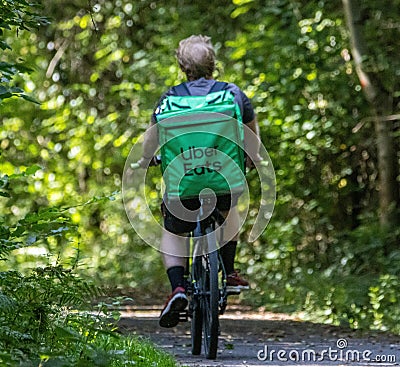 male riding his bicycle in the forest, looking back over his shoulder: Uber Eats Editorial Stock Photo
