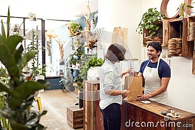 Male Sales Assistant In Florists Shop Serving Female Customer At Sales Desk Stock Photo