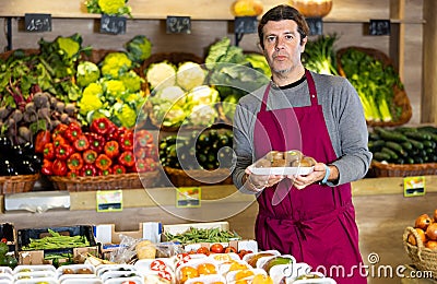 Male seller holding packaged kiwis standing in fruit and vegetable section of supermarket Stock Photo