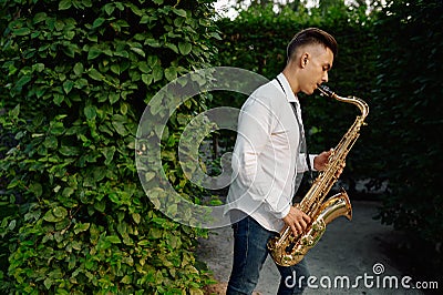 Male saxophonist plays on the alley in summer park Stock Photo