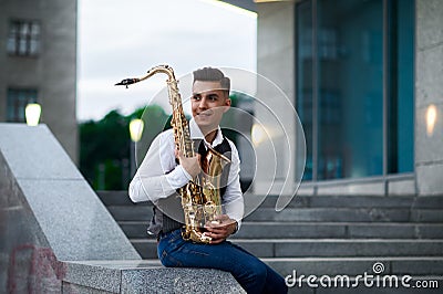 Male saxophonist poses at the stairs on street Stock Photo