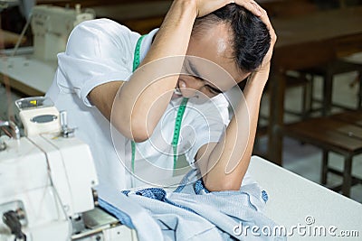 Male seamstress looked down with her head feeling depressed while sewing Stock Photo