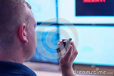 Male security guard operator talking on the phone, calling in the alarming event to the external team of field force agents Stock Photo