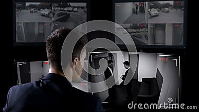 Male security operator watching surveillance cameras, illegal business deal Stock Photo