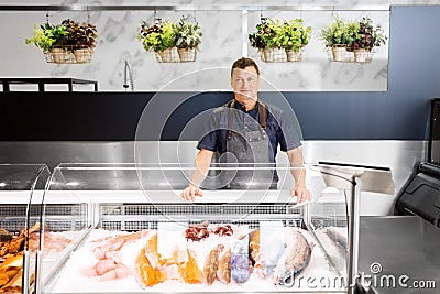 Male seller with seafood at fish shop fridge Stock Photo