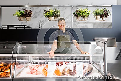 Male seller showing seafood at fish shop fridge Stock Photo