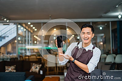 male shop assistant with hand gesture presenting mobile phone in furniture store Stock Photo