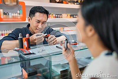 male shopkeeper changing the vape cotton in front of the vaping woman Stock Photo