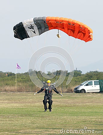 Male skydiver making safe landing landing on grass with open bright colourful parachute. Editorial Stock Photo