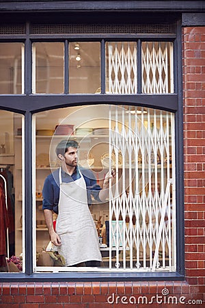 Male Small Business Owner Pushing Back Security Grill And Opening Shop Stock Photo
