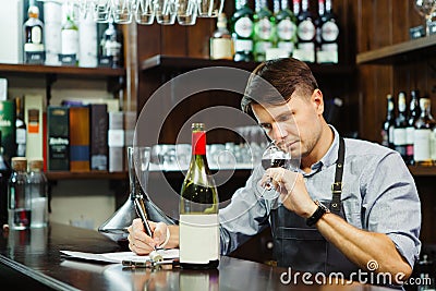 Male sommelier tasting red wine and making notes at bar counter Stock Photo