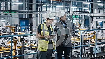Male Specialist and Female Car Factory Engineer Talking and Working on Laptop and Tablet Computers Stock Photo