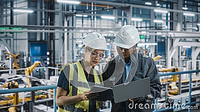 Male Specialist and Female Car Factory Engineer Talking and Working on Laptop and Tablet Computers Stock Photo