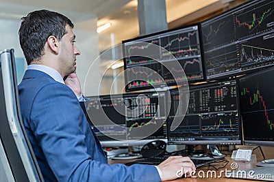 Stock broker trading online watching charts and data analyses on multiple computer screens. Stock Photo