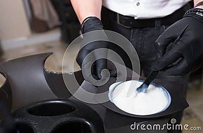 Male Stylist in gloves preparing color cream for dying hairin a container, a mask for treatment procedure in beauty salon. Stock Photo