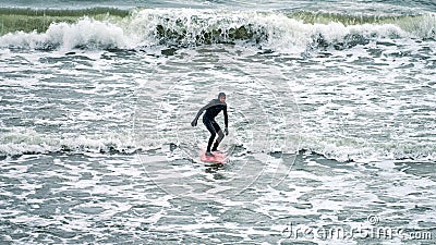 Male surfer in black swimsuit with red surfboard in sea waves Editorial Stock Photo