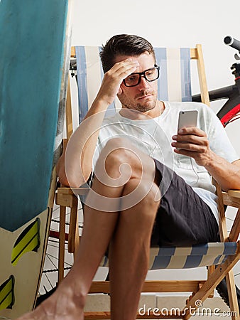 Male surfer and cyclist on self-isolation, sits on chair, quarantine at home. Stock Photo
