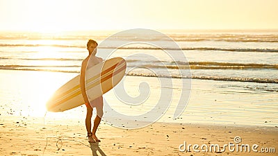 Male surfer walking on beach with surfboard at sunrise Stock Photo