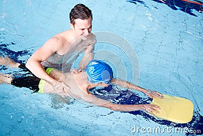 Male Swimming Coach Giving Boy Holding Float One To One Lesson In Pool Stock Photo