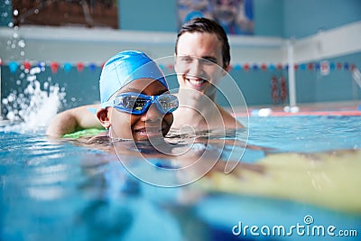 Male Swimming Coach Giving Boy Holding Float One To One Lesson In Pool Stock Photo