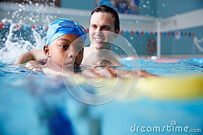 Male Swimming Coach Giving Boy Holding Float One To One Lesson In Pool Stock Photo