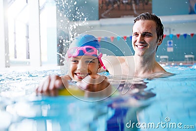 Male Swimming Coach Giving Girl Holding Float One To One Lesson In Pool Stock Photo