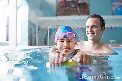 Male Swimming Coach Giving Girl Holding Float One To One Lesson In Pool Stock Photo