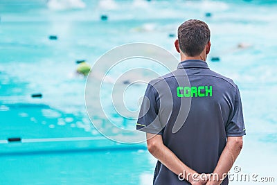 male swimming coach standing by the swimming pool watching swimmers racing by Stock Photo