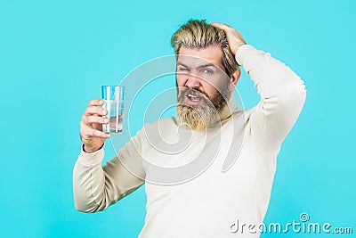 Male taking a pill with a glass of water. Man take some pills, holds glass of water, isolated on blue. Berded man taking Stock Photo