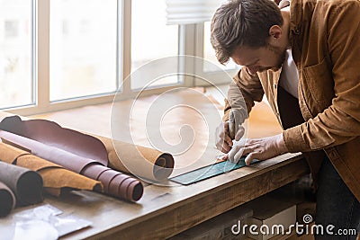 Male tanner making cutting scheme of bag working at leather workshop. Handcrafted creating Stock Photo