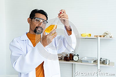 Male teacher in white lab coat with safety glasses looking serious at mixed chemical liquid in bottle and pipette Stock Photo