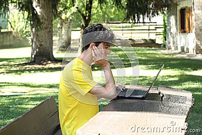 Male teenager uses a computer outside in a garden with copy space for your text Stock Photo