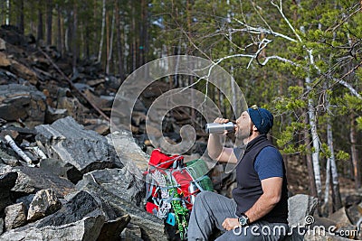 Male tourist drinks clear water from a bottle in the rocky forest. Stock Photo