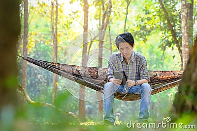 Male tourists resting on hammock listening to music in the national park Stock Photo