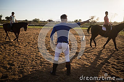 Male trainer guiding young women in riding horse Stock Photo