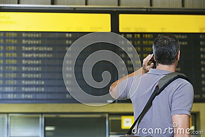 Male Traveler Using Cellphone By Flight Status Board Stock Photo