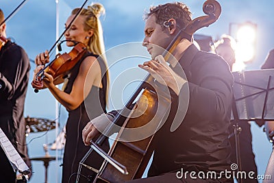 Male violoncellist playing in orchestra at outdoor concert Stock Photo
