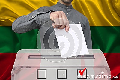 Male voter drops a ballot in a transparent ballot box against the background of the national flag of Lithuania, concept of state Stock Photo