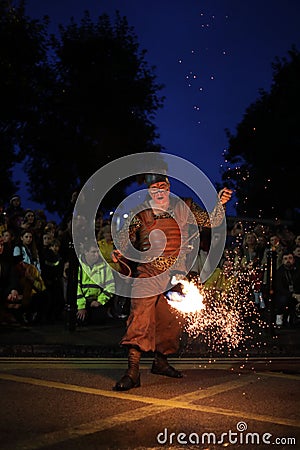 Male wearing a colorful costume and holding a flaming prop performing a fire show Editorial Stock Photo