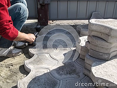 A male worker beats a rubber mallet on paving slabs in the patio near the fence. The process of laying paving slabs in the yard or Stock Photo