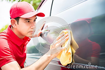 Male worker cleaning and looking at car door seriously Stock Photo