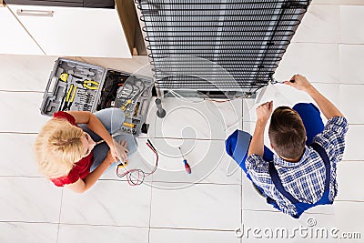 Male Worker Repairing Refrigerator In Kitchen Room Stock Photo