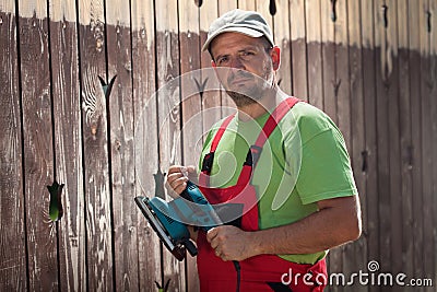 Male worker with vibrating sander in front of old wooden fence Stock Photo