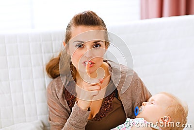 Mama holding sleeping baby and showing shh gesture Stock Photo